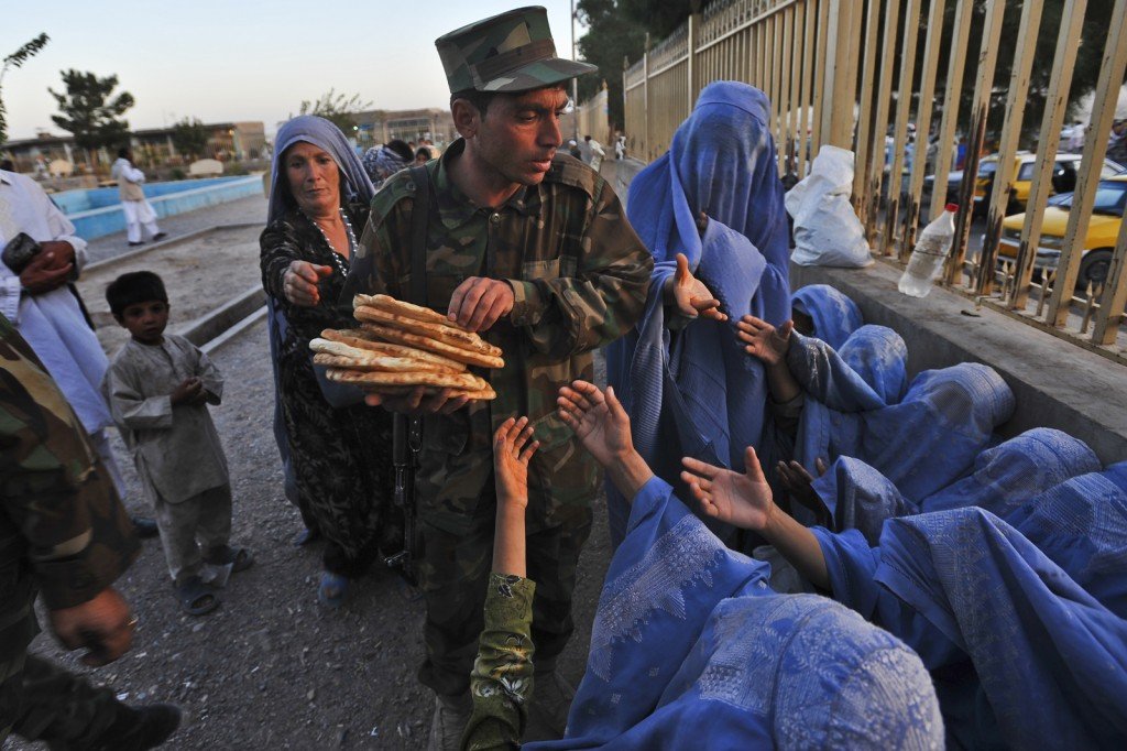 Afghan widows and poor women throng the outside of the Khuj Shahib Abdullah Ansar Shrine in Herat as they ask for money and food donations from the people. Afghan police officers typically collect donations from Afghans and hand them out to the women. Herat, Afghanistan, Oct 2, 2009. Woman screaming holding bread, saying I have no money, i have nothing to feed my children!' Shebnam, 40, she lives in Painow, and has five children. her husband died of heart problems six years ago, and she washes clothes and begs on fridays to make money. Man handing out money to widows: Mansour Ahmad, 23, from herat. shopkeeper.  Man in uniform handing out bread; Gulam Farouq, 23, an ANA solider Afghan women visit the grave of a relative in the Farah section of the cemetery outside the shrine. it is called the Ana Daragi cemetery